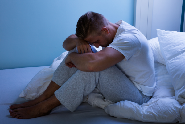 Frustrated man sitting alone in bed with his head on his knees