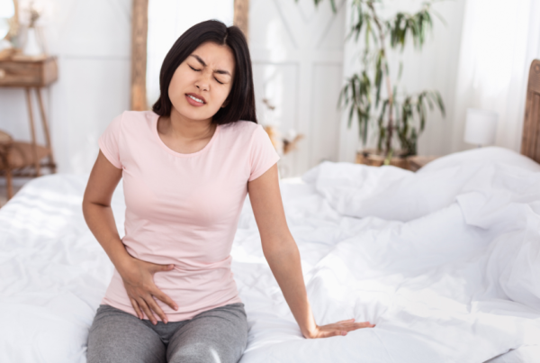 person sitting on a bed holding their lower abdomen in pain