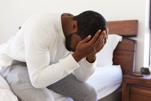 Man sitting on the edge of a bed holding his face in his hands