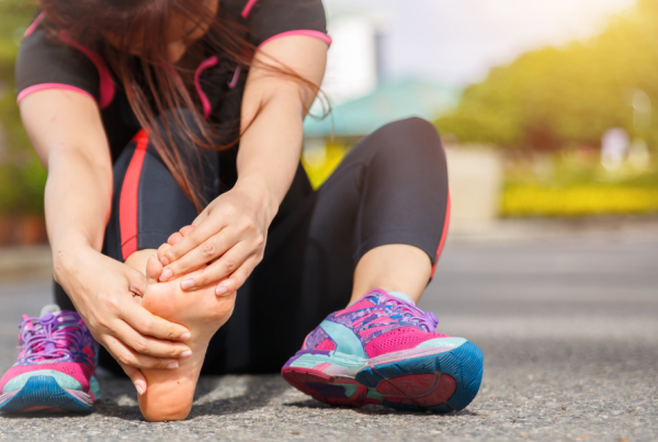 Woman in athletic wear sitting and holding her bare foot in pain