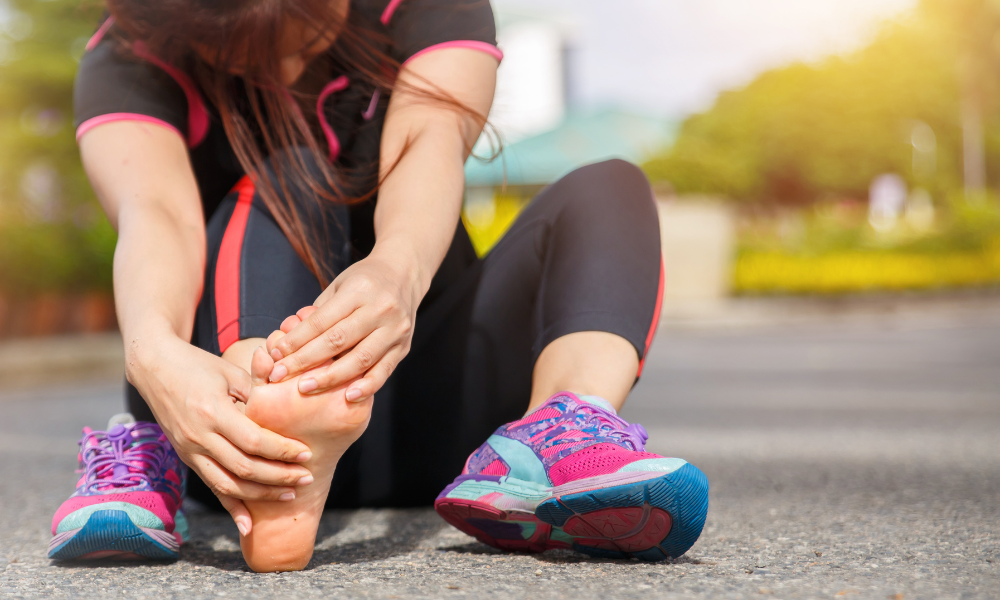Woman in athletic wear sitting and holding her bare foot in pain