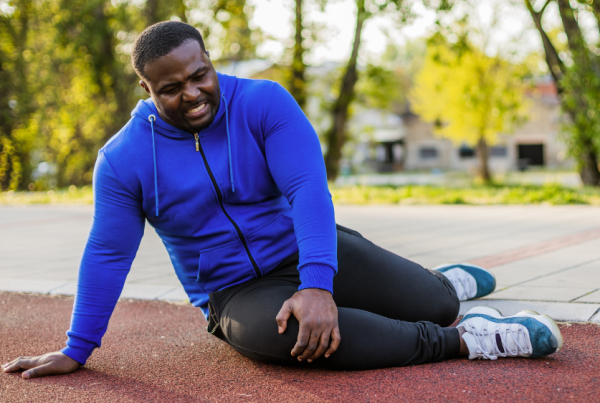 Man in athletic clothing sitting on the ground and holding his knee