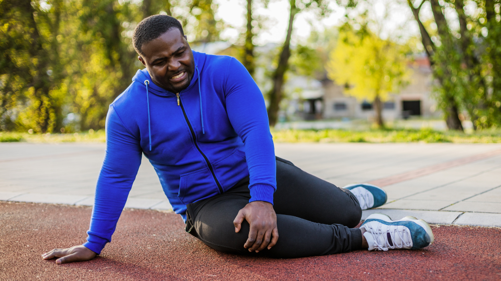 Man in athletic clothing sitting on the ground and holding his knee
