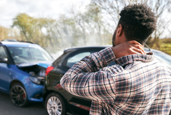 Person holding their neck as they look at two cars involved in an accident