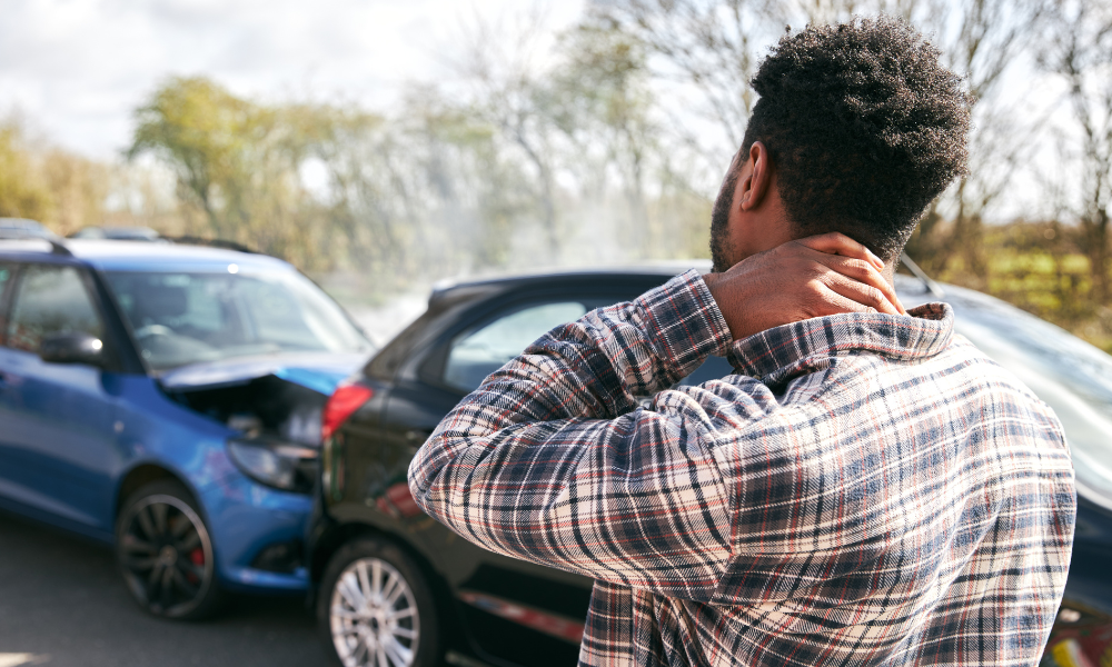 Person holding their neck as they look at two cars involved in an accident